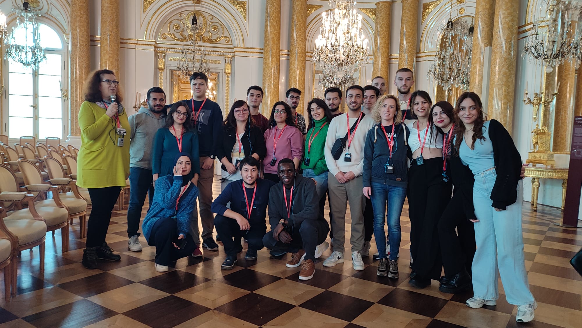 Studenci Erasmus+ pozują w sali z ozdobnymi złotymi kolumnami i żyrandolami w Warszawie.